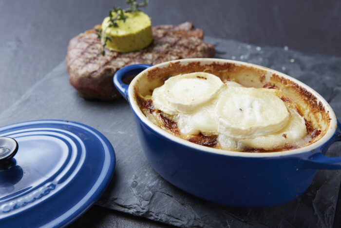 Überbackenes Kartoffelgratin an gegrilltem Steak „Café de Paris“ mit französischer Ziegenkäserolle